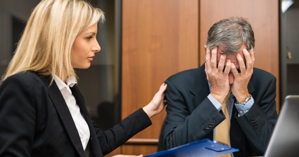 A man and woman in business attire sit at a desk with a laptop, discussing wrongful death lawsuits in Texas.