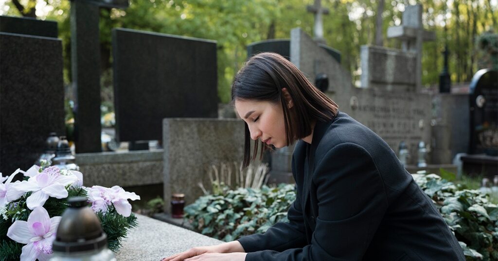 A woman in a suit kneels at a grave, reflecting on a wrongful death claim with a somber expression.