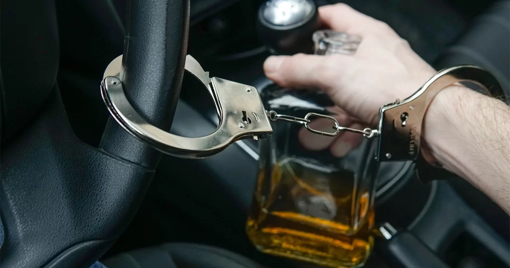 Handcuffed driver with alcohol bottle, symbolizing DUI felony