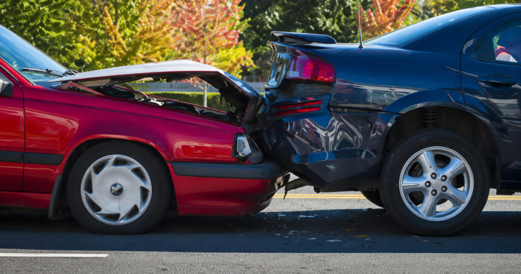 Rear-end collision between two cars on a road, with visible front and rear damage.