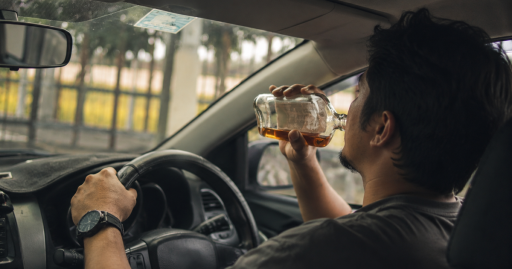 Man in the driverโs seat drinking from a bottle inside a car.
