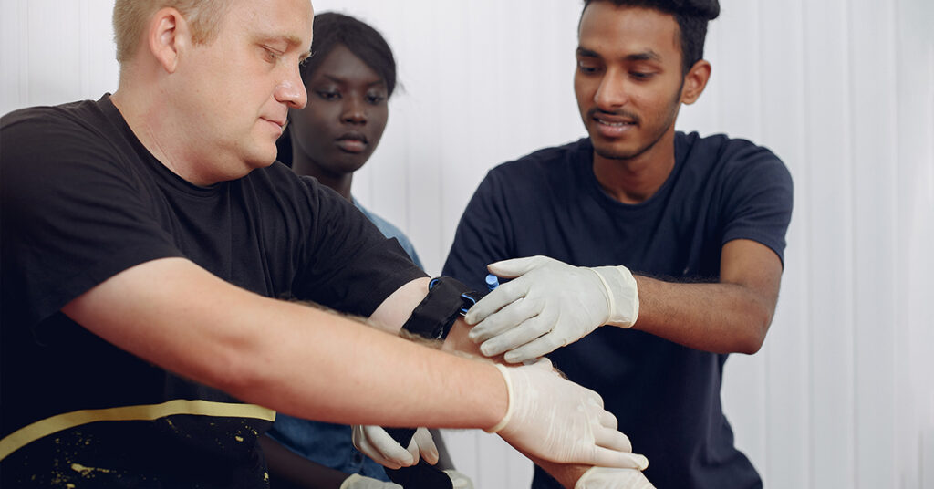 Medical personnel applying a tourniquet to a man's arm.